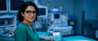 Female surgeon in green scrubs and glasses smiling confidently in modern operating room with medical equipment. Healthcare professional ready for surgery.