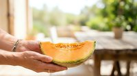 Ripe orange melon slice held in male hands outdoors in sunny garden setting, fresh produce for healthy eating and summer harvest themes.