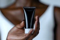 African American woman's hand holding black cosmetic tube against blurred background. Close-up view of skincare or beauty product packaging demonstrates luxury presentation.