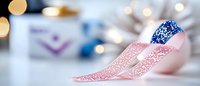 Pink and blue decorative ribbons with sparkly texture lying on white surface with soft bokeh lights and gift boxes in blurred background for celebrations.