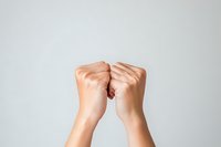 Female hands clenched in fists facing each other against light background, expressing tension, conflict, confrontation, or internal struggle concept.