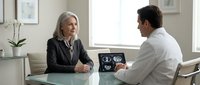 Senior Caucasian businesswoman consulting with male doctor about medical results in modern office setting for healthcare and professional services.