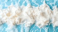 White foam soap bubbles on bright turquoise blue water surface with swirling patterns and dynamic texture creating abstract background for spa and hygiene concepts.