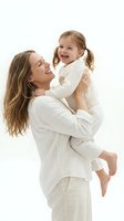 Happy Caucasian mother holding laughing toddler daughter in white clothing on clean background for family lifestyle and parenting concepts.