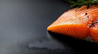 Fresh raw salmon fillet with rosemary sprig and peppercorns on dark slate background, macro view with copy space for culinary and food design.