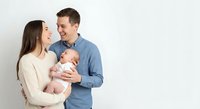Happy young Caucasian parents holding newborn baby against white background. Family portrait with mother, father and infant child for parenting concepts.