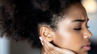 Young African American woman with natural curly hair and closed eyes in serene expression, touching face gently against soft blurred background. Wellness and self-care concept.