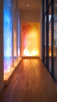 Modern hallway with illuminated color-changing wall panels creating dramatic lighting effects against wooden flooring, combining warm orange and cool blue tones in contemporary design.