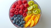 Fresh colorful fruit bowl with raspberries, blueberries, kiwi and orange slices arranged in sections, top view on white background for healthy eating concept.
