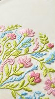 Delicate hand embroidered floral pattern with pink flowers and green leaves on cream fabric showcasing traditional needlework craftsmanship for textile design.