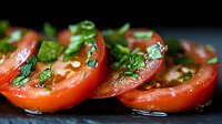 Fresh red tomato slices garnished with chopped herbs, olive oil and seasonings on dark background, close up view of appetizing Mediterranean cuisine.