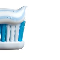 White toothbrush with blue bristles and striped toothpaste isolated on white background for dental hygiene and oral care design projects.