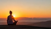 Woman meditating in lotus pose on mountain peak at sunrise with golden sky and layered hills creating peaceful mindfulness scene for wellness and spiritual practice.