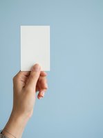 Hand holding blank white card against blue background, suitable for business branding, marketing mockups, and promotional designs.