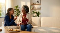 African American mother and teenage daughter sharing healthy snacks while having intimate conversation on modern living room sofa with natural lighting.
