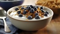Fresh blueberries and crunchy granola topped on creamy yogurt in white ceramic bowl, morning breakfast setting with natural lighting and wooden surface.