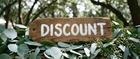 Rustic wooden discount sign surrounded by lush green eucalyptus leaves in a natural outdoor garden setting, perfect for sale promotions.
