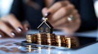 Small house model on stacks of gold coins with businesswoman hands in background, representing real estate investment, property market and mortgage concept.
