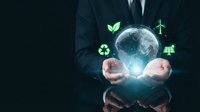 Businessman in suit holding glowing Earth globe with green renewable energy icons including wind turbines, solar panels, recycling symbols and leaves.