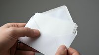 Hand holding stack of blank white business cards or note cards against gray background for mockup design templates and branding projects.