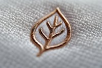 Elegant copper wire leaf design embroidered on light gray linen fabric, showing delicate metallic needlework details in macro photography view.