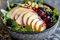 Fresh pear and berry salad with arugula greens and walnuts in gray ceramic bowl, close up view showing vibrant ingredients and textures.