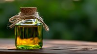 Glass jar with cork stopper and twine containing golden liquid on wooden surface against blurred green nature background, natural wellness concept.