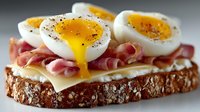 Gourmet open sandwich with soft-boiled eggs, prosciutto and cheese on multigrain bread. Breakfast toast with runny yolk and black pepper seasoning.