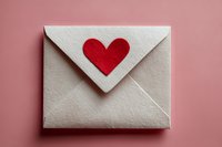 White envelope with red heart on pink background, symbolizing love message or romantic correspondence for Valentine's Day or anniversary celebration.