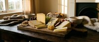 Artisanal cheese board with crackers and nuts on wooden table in cozy living room with fireplace and warm natural lighting for entertaining.