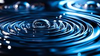 Water drop creating concentric ripples on dark liquid surface with blue illumination and bokeh light effects, macro photography showing surface tension dynamics.
