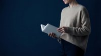 Young professional woman in beige sweater reading book against dark blue background with copy space for business education concepts.