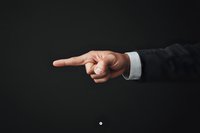 Male hand in business suit pointing finger to side against dark background, showing direction, leadership concept or accusation gesture.