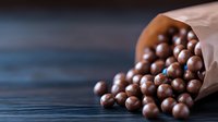 Chocolate balls spilling from paper bag onto dark wooden surface, creating appetizing composition with selective focus and copy space for food design.