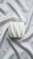 Geometric white candle with folded faceted design on draped fabric background, isolated for home decor, interior styling, and product photography use.