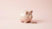Pink piggy bank with coins on pastel background for savings and financial planning concepts.