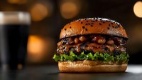 Juicy beef burger with melted cheese, crispy bacon, and fresh lettuce on sesame seed bun against dark background with bokeh lights. Food photography.