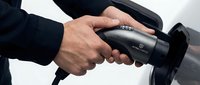 Professional businessman charging electric vehicle with modern charging cable at station for sustainable transportation and eco-friendly mobility solutions.