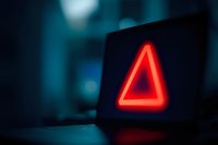 Glowing red triangle warning sign on dark background, creating atmospheric emergency alert in blurred blue environment.