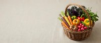 Fresh organic vegetables and herbs in wicker basket on neutral background for healthy eating and farm-to-table cooking concepts.