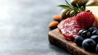 Gourmet charcuterie board with salami, fresh berries, nuts and herbs on rustic wooden serving platter for appetizer presentation and food styling.