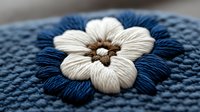Handmade embroidered flower with cream petals and brown center on blue fabric background. Traditional needlework craft technique for textile decoration projects.
