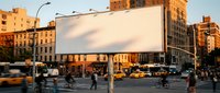 Large blank white billboard on busy urban street corner with yellow taxi cabs and pedestrians during golden hour sunset lighting for advertising mockup.