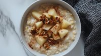 Creamy oatmeal topped with fresh diced pears, crunchy walnuts and cinnamon in white ceramic bowl on marble surface, healthy breakfast meal.