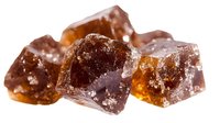 Brown sugar crystals with caramel color variations and translucent edges on white background, macro photography showing crystalline structure and light reflections.