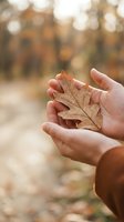 Child holding dried autumn oak leaf in hands with blurred fall forest background, seasonal nature exploration and outdoor activities.