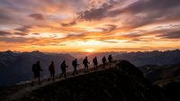 Group of hikers standing on mountain ridge at sunset, silhouetted against golden and purple sky with distant alpine peaks, outdoor adventure and teamwork concept.