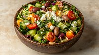 Fresh Mediterranean salad with feta cheese, olives, cucumber, tomatoes, bell peppers and herbs in rustic ceramic bowl on beige background. Healthy eating.
