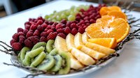 Fresh fruit platter with sliced oranges, kiwi, banana and raspberries arranged on decorative plate for healthy breakfast, party catering or dessert presentation.