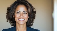 Mixed race woman with wavy dark hair and bright genuine smile against blurred background, professional headshot style portrait for business and corporate use.